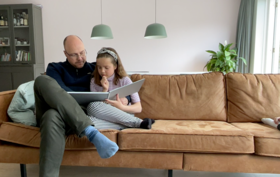 Vader en dochter lezen samen een boek. Ze zitten op de bank.